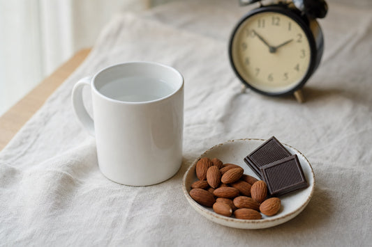 Tasse d'eau, amandes et chocolat noir devant un réveil analogique